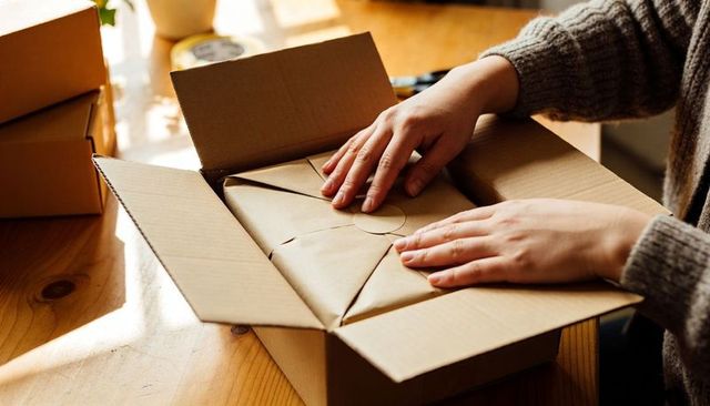 Hands Wrapping Sustainable Kraft Parcel in Cardboard Box for Small Business Shipping
