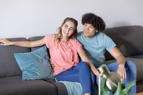 Young couple sitting on gray sofa cuddling, smiling and relaxing in cozy living room