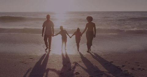 Family Walking Toward Sunset on Beach Holding Hands Silhouette with Long Shadows