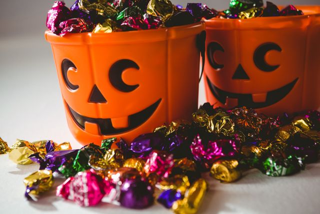 Orange Halloween buckets filled with multicolored chocolates, perfect for festive decorations, trick-or-treat events, and holiday parties. Ideal for use in advertisements, social media posts, and promotional materials related to Halloween celebrations.