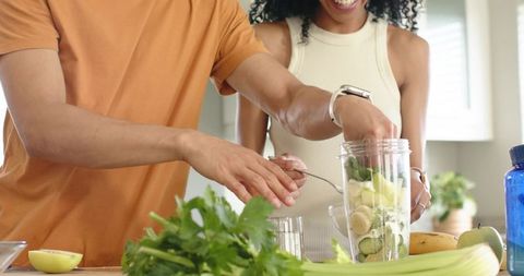 Diverse couple preparing healthy green smoothie together in bright home kitchen counter