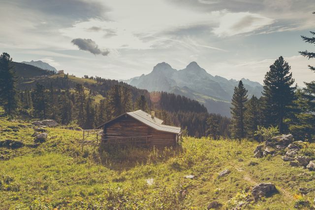 Rustic wooden cabin situated in a scenic mountain area. Surrounded by trees with rugged mountains in the background, creating a tranquil and picturesque outdoor setting. Ideal image for conveying themes of nature, peace, escape, adventure, and wilderness exploration.