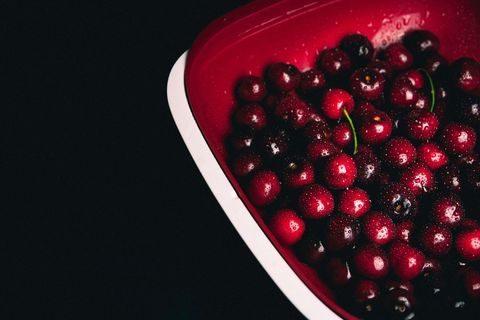 Fresh ripe berries in red colander against dark cherry background