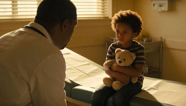 Doctor comforting child on exam table holding teddy bear during pediatric exam