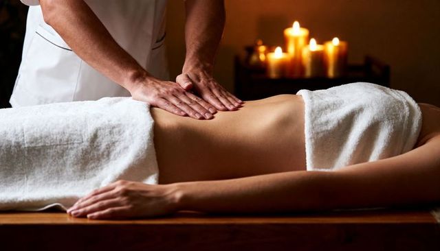 Therapist massaging bare back during candlelit spa treatment for deep relaxation