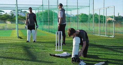 Teen fastening protective pads in cricket nets during coach-led training session