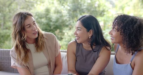 Diverse women chatting on porch while sharing tablet during sunlit outdoor gathering