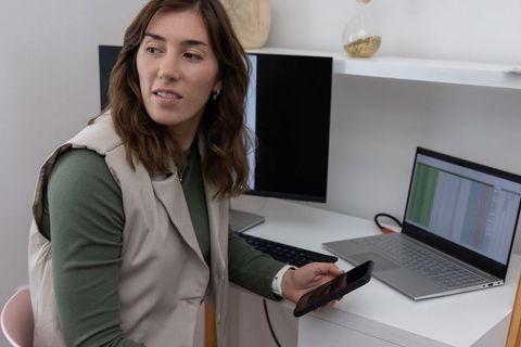Remote professional reviewing spreadsheet on laptop while holding smartphone in home office