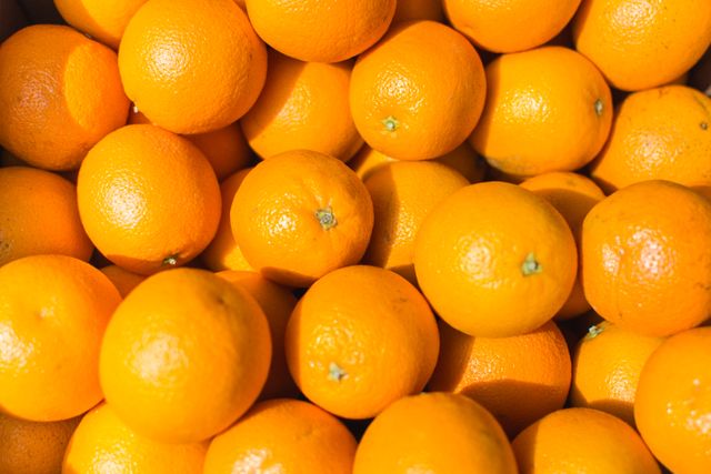 Close-up view of fresh ripe oranges in bright lighting, showcasing their vibrant color and healthy appeal. Suitable for use in advertisements promoting health, citrus fruit products, grocery store marketing materials, and dietary blogs emphasizing vitamin C and healthy eating.