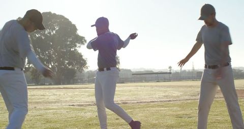 Three baseball teammates stretching and warming up on sunlit backlit field at dawn