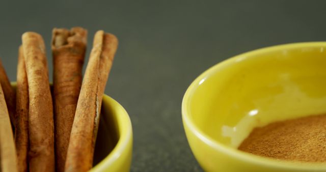Cinnamon sticks in a bowl and ground cinnamon in a small yellow bowl. Image evokes senses of winter cooking and warm baking spices. Suitable for food blogs, culinary websites, and spice product showcase.