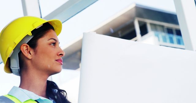 A young Caucasian female engineer wearing a safety helmet looks confidently at a construction site, with copy space. Her professional attire and focused gaze reflect her role in overseeing the project's progress.