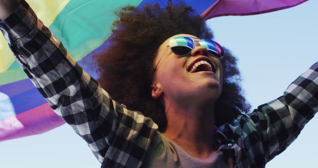 Joyful person celebrating with rainbow flag under clear blue sky - Download Free Stock Images Pikwizard.com