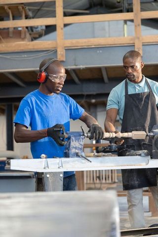 African american mentor teaching apprentice woodturning on lathe wearing safety gear