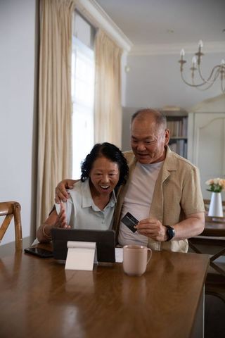Senior asian couple celebrating online purchase using tablet and credit card at home