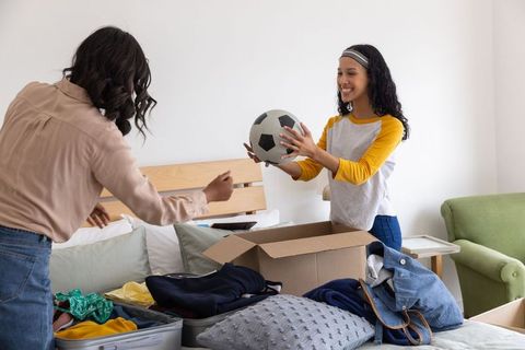 Mother and daughter unpacking together receiving soccer ball in cozy home bedroom
