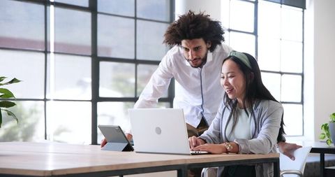 Diverse Team Collaborating in Modern Office with Laptops and Tablets