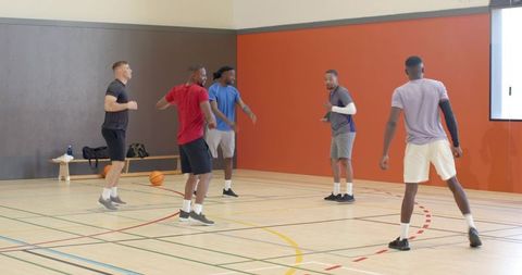 Five players practicing defensive stance and team drill during indoor basketball training session