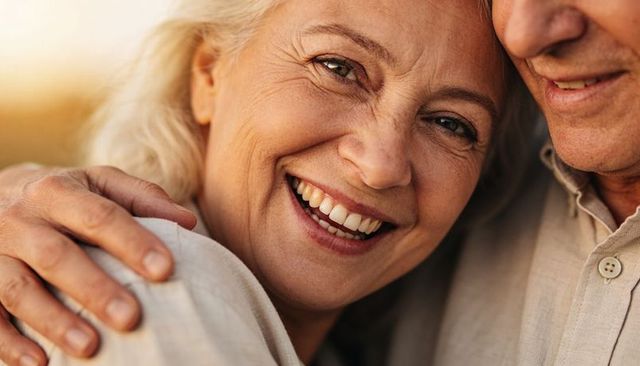 Sunlit senior couple embracing at golden hour, joyful smiling woman close-up