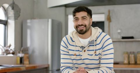 Indian man leaning on kitchen counter smiling in cozy modern kitchen interior