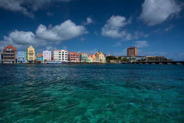 This scenic shot captures a row of vibrant, colorful buildings along a waterfront under a clear blue sky. Ideal for travel brochures, tourism advertisements, website banners or social media posts highlighting tropical destinations or aimed at promoting vacations.