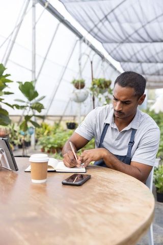 Indian nursery owner planning business and taking notes in greenhouse workspace