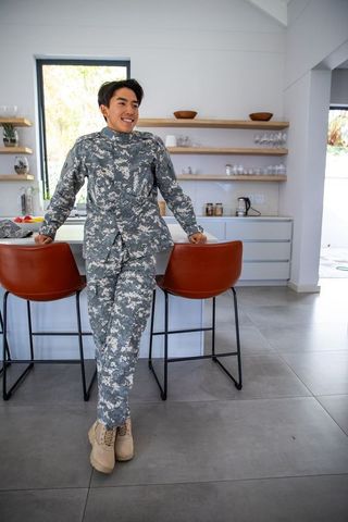 Asian servicemember wearing gray digital camouflage leaning on modern kitchen island smiling