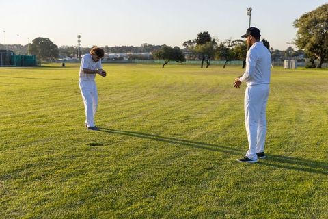 Two cricketers practicing on sunlit grass during golden hour coaching catching drill