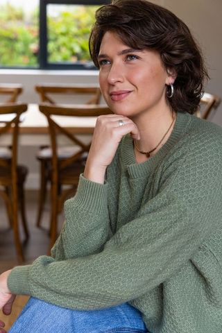 Contemplating woman in green knit sweater looking out window in cozy dining interior