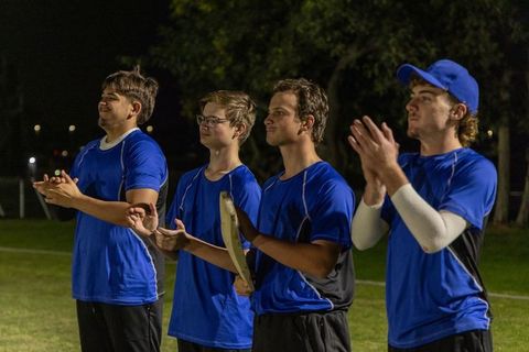 High school baseball teammates clapping on grass field at night while holding bat