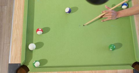 Overhead green pool table with scattered balls, cue stick and player's hand aiming