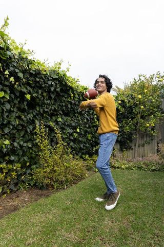 Teen throwing football in backyard garden with ivy-covered fence and lemon tree