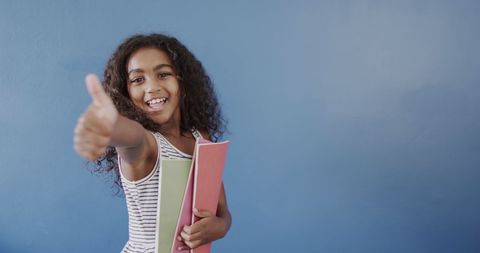 Cheerful young girl giving thumbs up with notebook