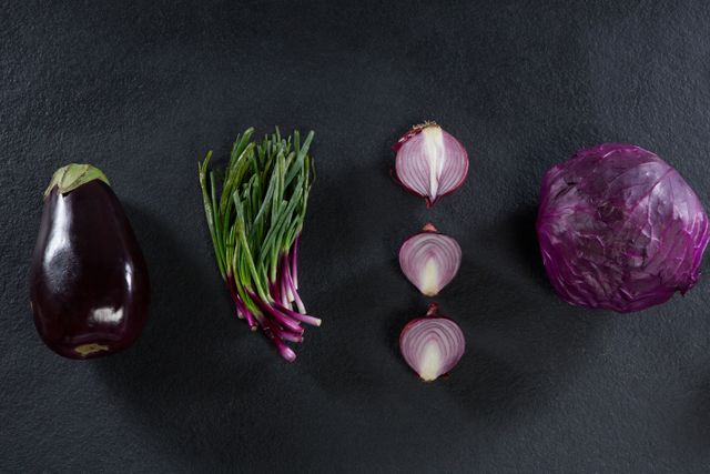 Assorted fresh vegetables including eggplant, chives, red onion, and purple cabbage arranged on a black background. Ideal for use in cooking blogs, healthy eating promotions, vegetarian and vegan recipe websites, and nutritional guides.