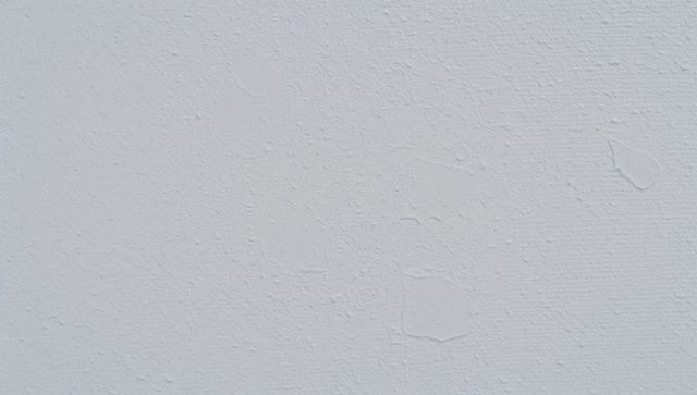 Closeup peeling plaster wall with patch repairs and cracks, neutral textured surface