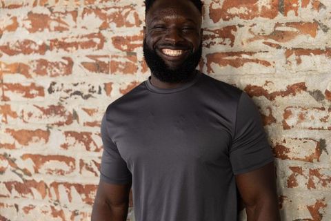 Smiling african american man leaning on peeling brick wall wearing dark-gray tee, septum ring