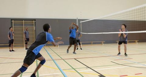 Diverse teen boys practicing volleyball drill in school gymnasium for team training