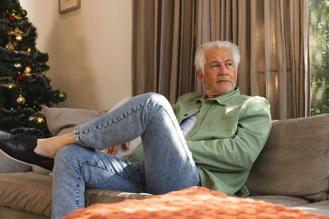 Senior man relaxing on sofa by christmas tree in bright living room