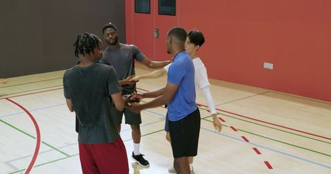 Male teammates joining hands before basketball practice on indoor court, showing teamwork