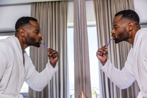 Mature african man brushing teeth at mirror in white bathrobe morning personal care
