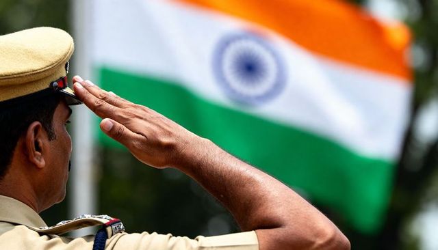 Khaki uniformed Indian police officer saluting tricolor flag at national ceremony