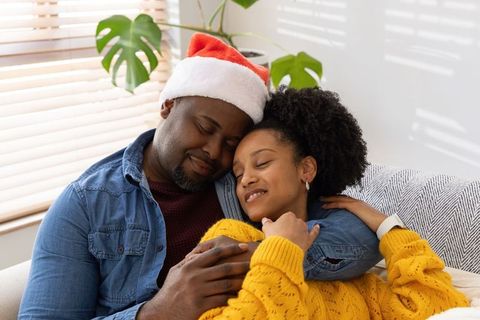 Cozy holiday cuddling african american couple on sofa wearing santa hat and sweater