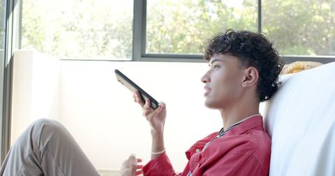 Young Man Relaxing at Home Using Smartphone Voice Command Feature