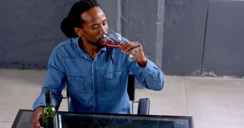 Man in denim shirt tasting red wine at modern desk