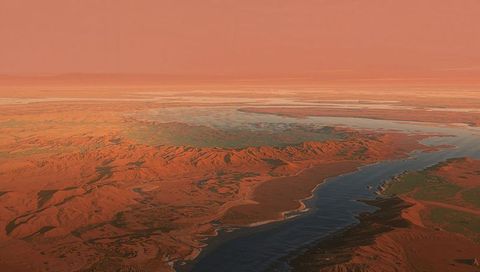 Meandering dark-blue river cutting through expansive red desert canyon at low sunlight