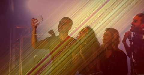 Friends taking selfie on stage under warm diagonal concert lights celebrating nightlife energy