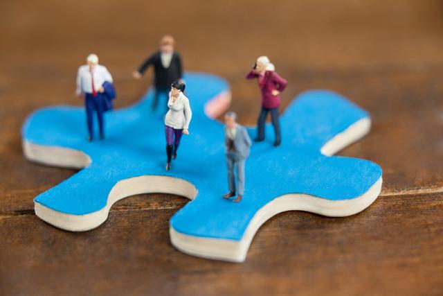 Miniature figures of people standing on top of a blue jigsaw puzzle piece, representing concepts like teamwork and collaboration. Ideal for illustrating business strategies, problem-solving, and the interconnectedness of team members in achieving common goals.
