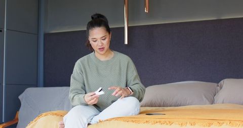 Woman examining gadget on bed in cozy modern bedroom