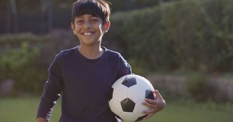 Smiling boy holding soccer ball on green lawn
