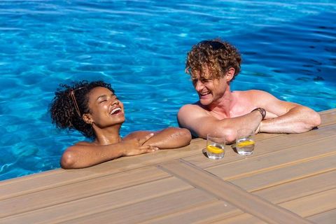 Mixed-race couple laughing and relaxing at turquoise pool deck with lemon drinks